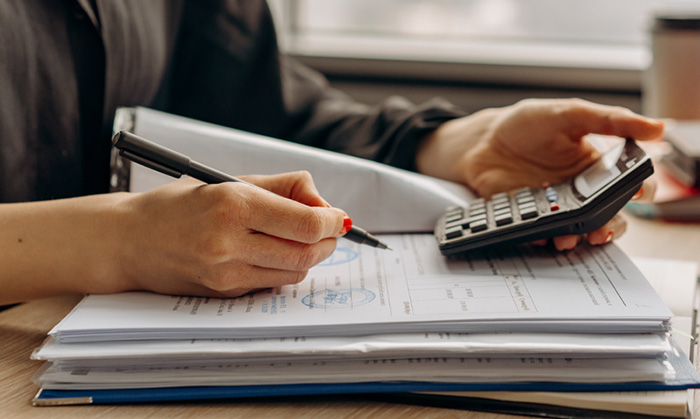 A person does paperwork and uses a calculator.